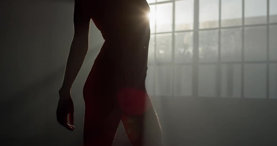 A female posing standing up in a dark room with sunlight shining in the window