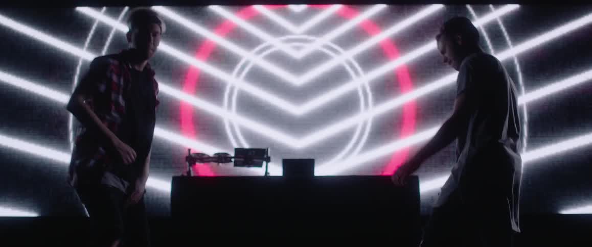 Two men dance in front of a light screen
