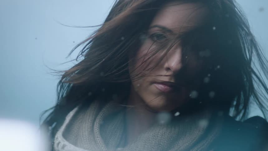 A young woman stands in a snowy environment as the wind blows her hair