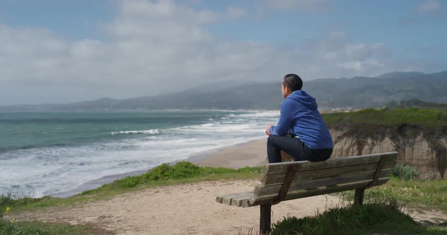 A man sits on a bench and looks out over the ocean