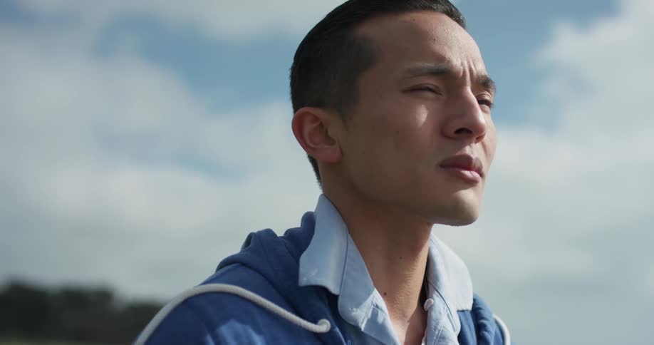 An asian man looks off into the distance while on a stroll during a windy day