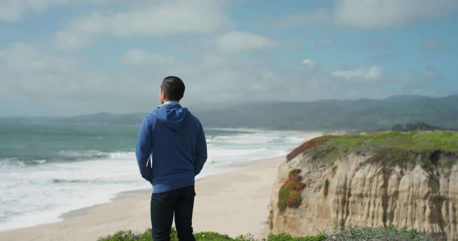 A man in a blue jacket stands on a beach