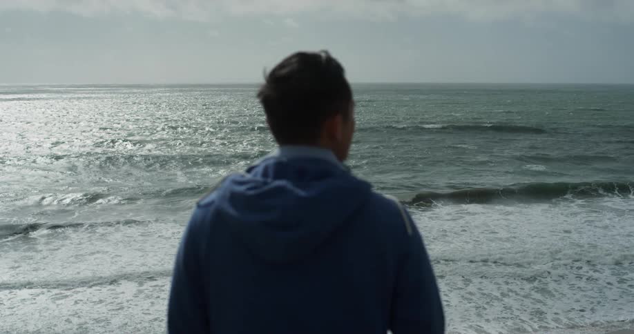 A man stands on a beach and stares out across the ocean