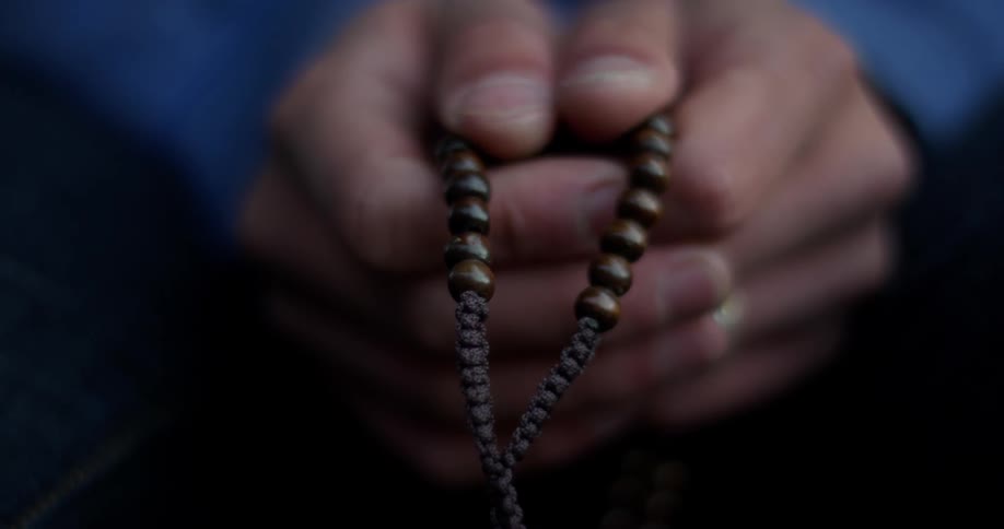 A man tightly clutches a string of beads