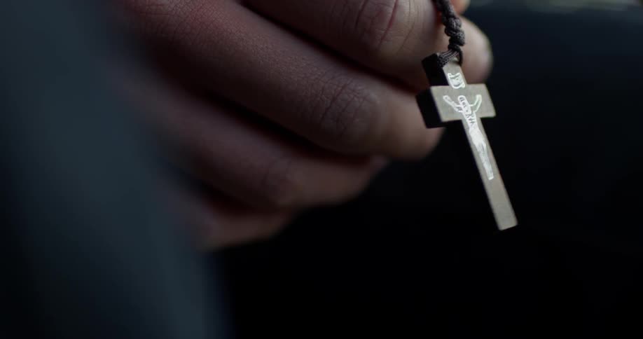Man holds wooden cross necklace during daylight