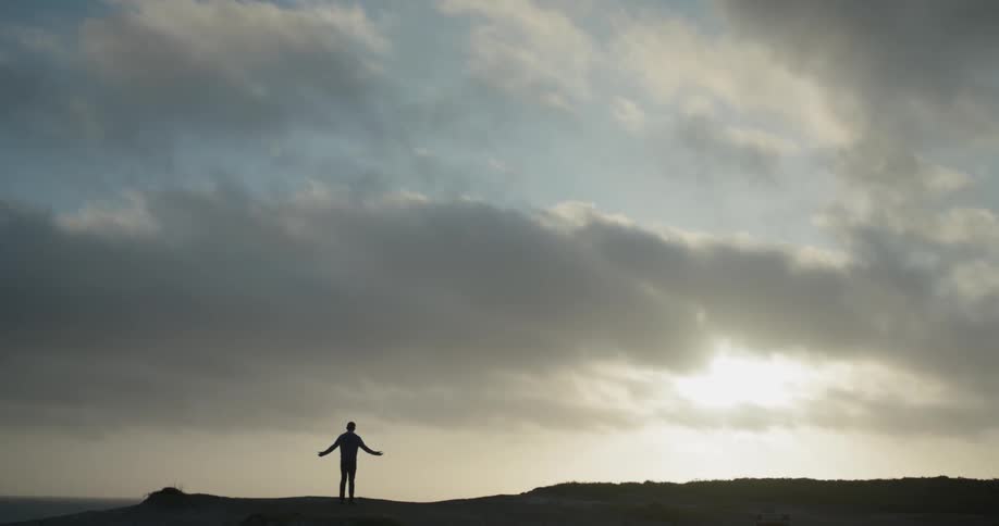 A man stands on a ridge with his arms stretched out to his sides