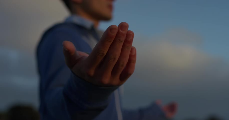 A man in a blue jacket stands outside with his arms stretched out to his side