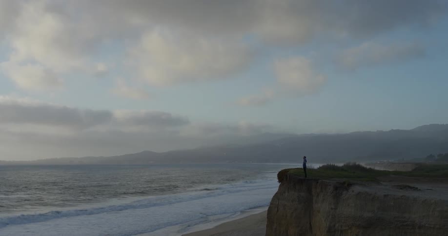 A person approaching the edge of a cliff overlooking a cliff and opening his arms wide