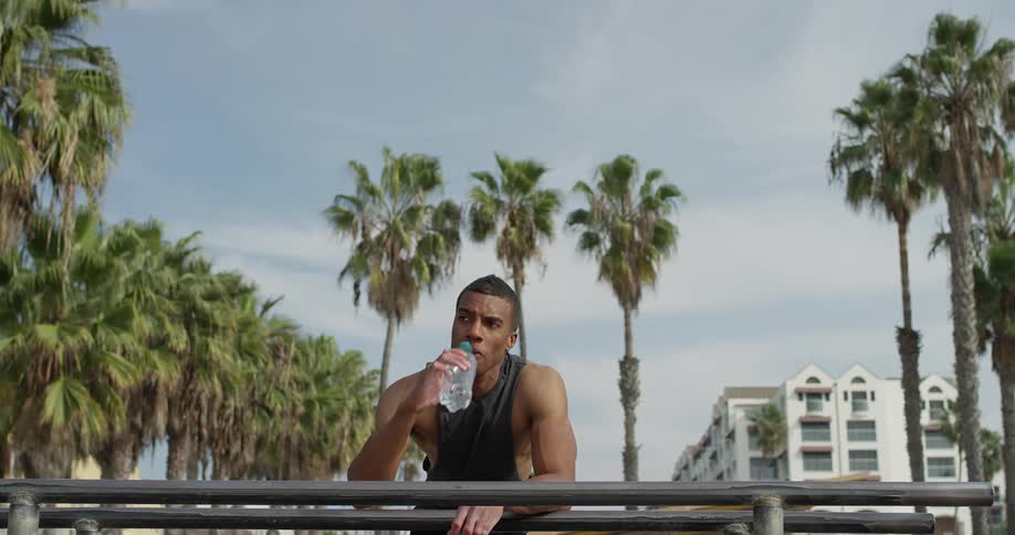 A man takes a drink of water as hes leaning on a railing