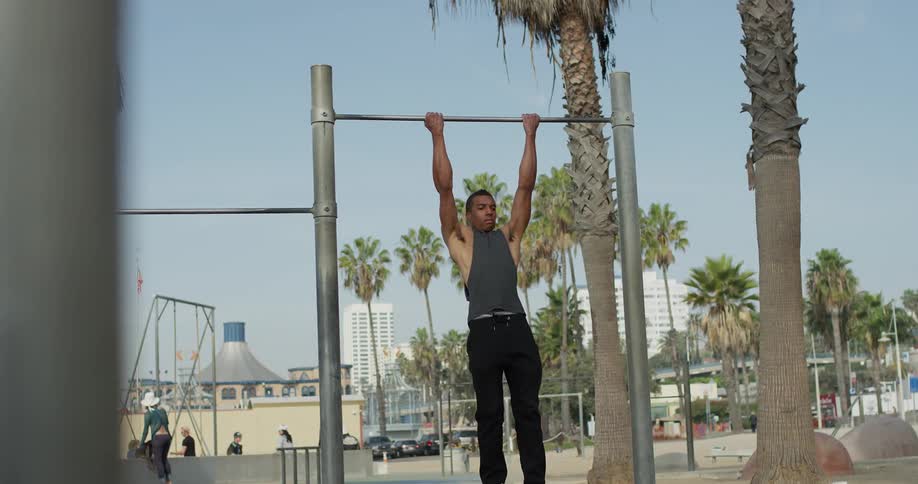 A young man does pull ups at a park