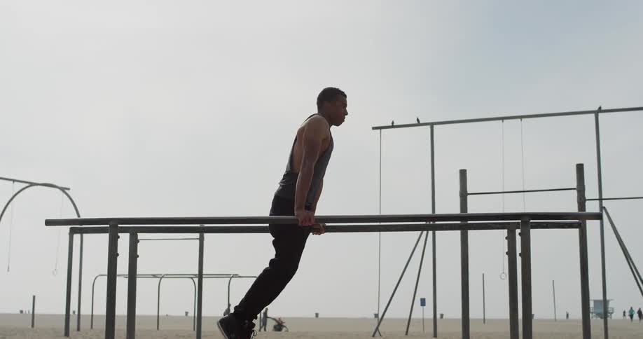 A man lifts himself on parallel bars and swings his legs