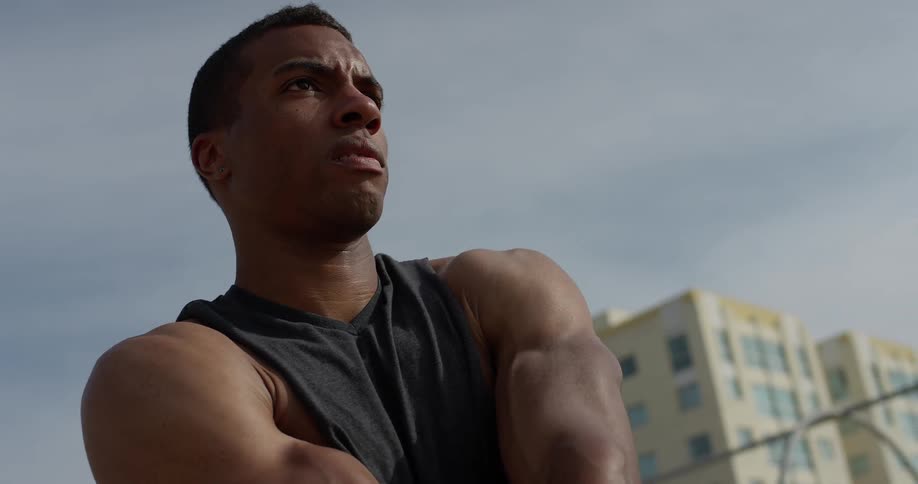A male in a vest warms up his upper body muscles in an urban area