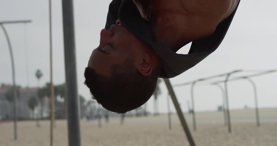 A young black man exercising on still rings on a beach