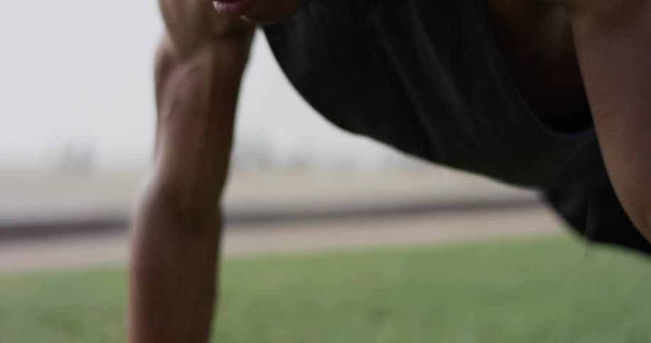 A black man does push ups on a plot of grass near the beach