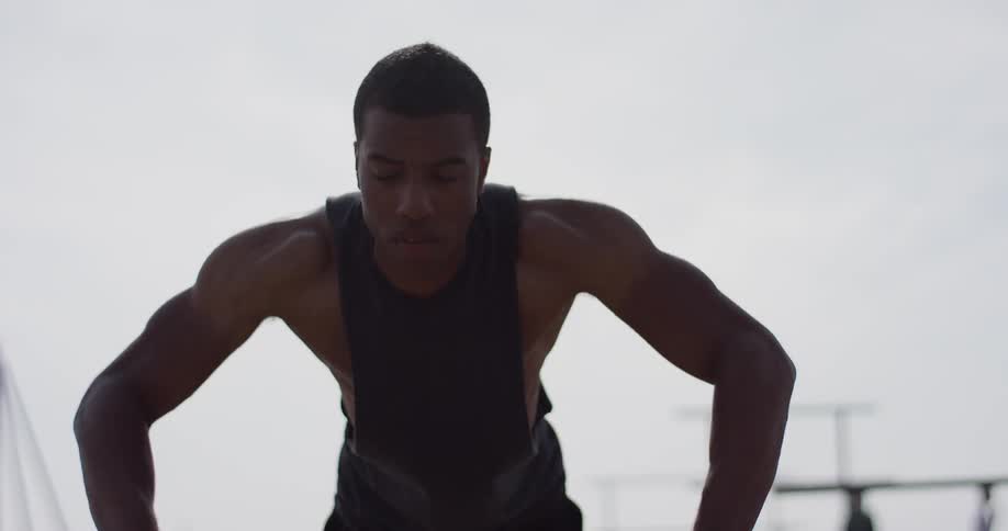 A young black man does push ups outside