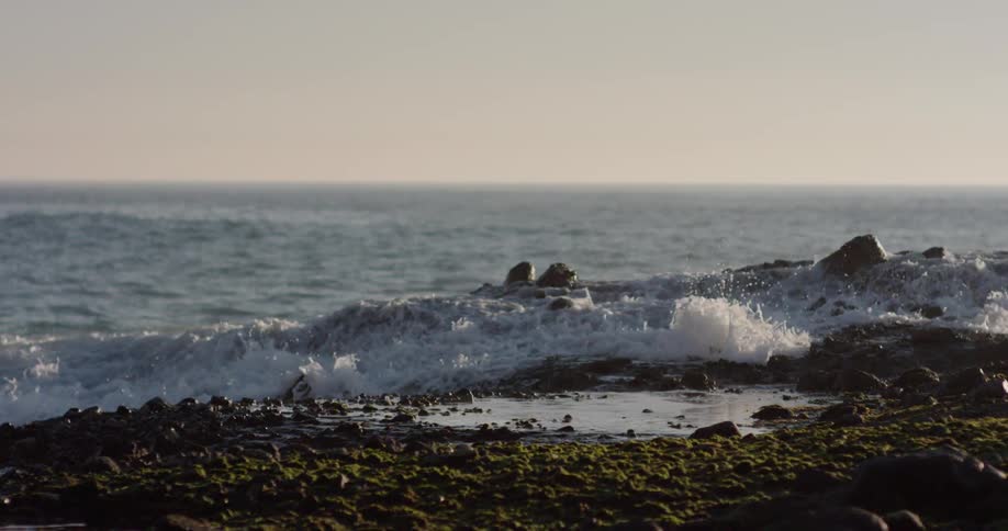 Waves crash over the rocks under a cloudy sky