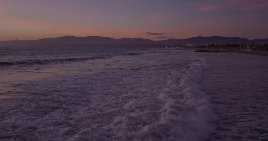 An aerial view of ocean waves landing on an empty beach at dusk