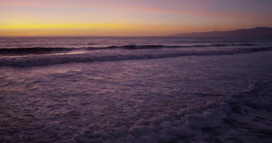 Several sets of waves wash towards the shore and crumble in foamy water as they wash upon the beach
