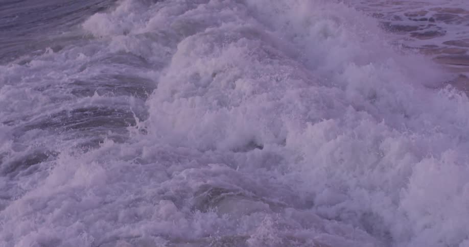Waves crash against the shore making a lot of foam at sunset