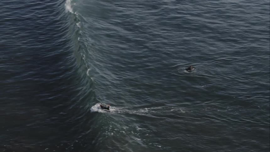 A wave passes a group of surfers floating in the water