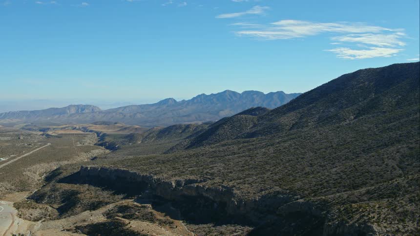 Dirt trails run through hills with a mountain range in the horizon