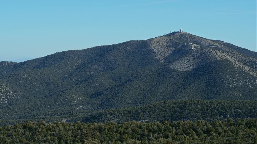 A large hill covered in trees under a light blue sky