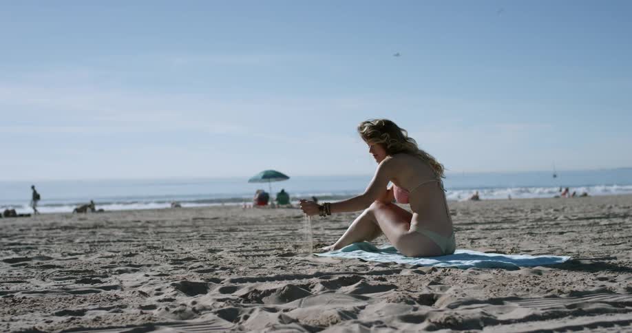 Young woman wearing bikini sits on towel on beach