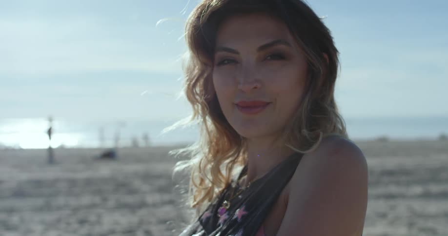 A woman looks into the camera while standing on a beach