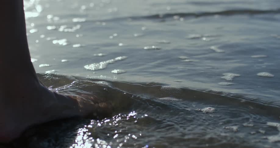 A woman barefoot walking on the shallow beach water