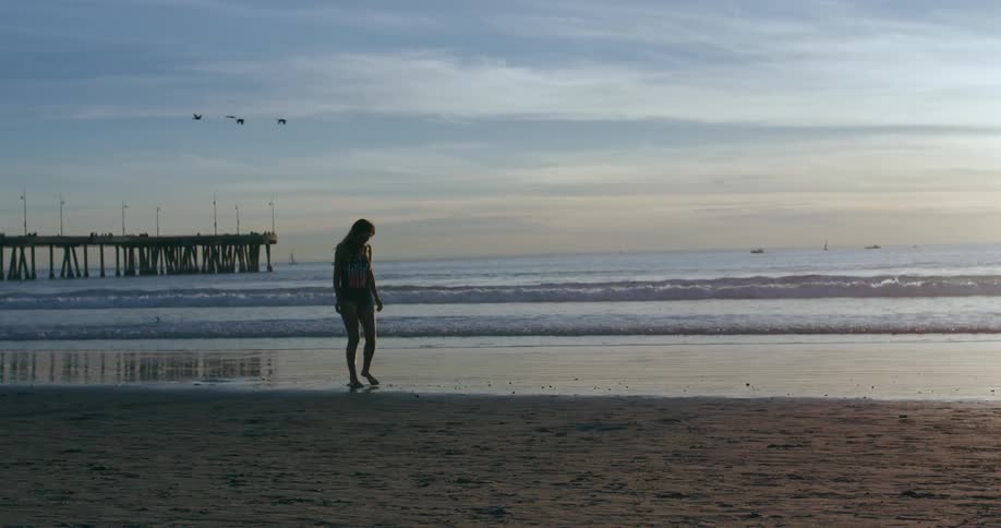 A woman in a bikini draws with her toes in the sand on the ocean shore
