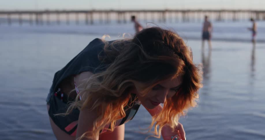 A woman picks up a shell on the beach
