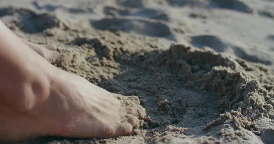 A person running their bare feet through sand