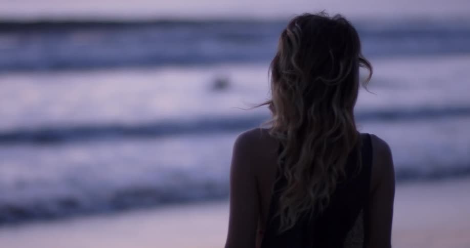 A woman on the beach standing watching the ocean and playing with her hair