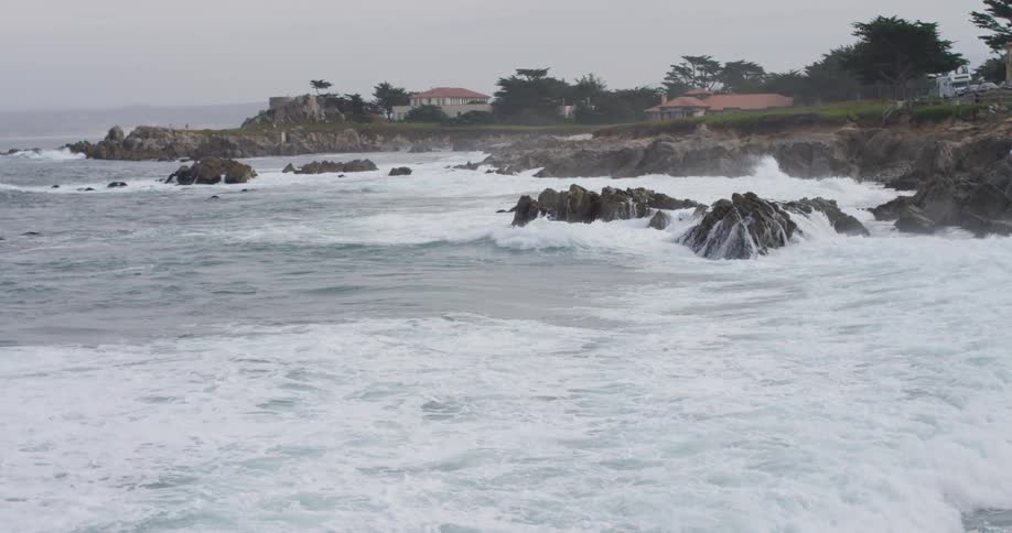 Waves crush against shore making lots of foam on a cloudy day