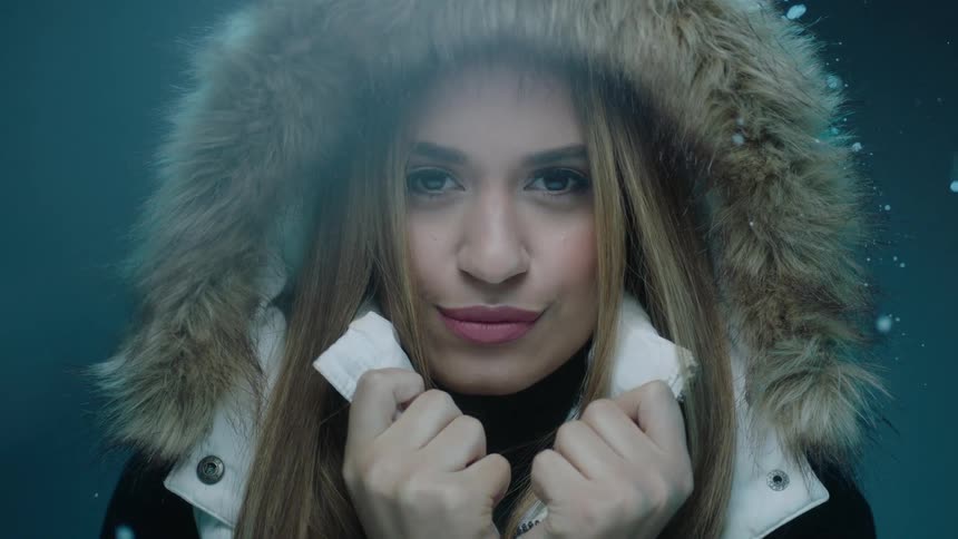 A young woman is holding her shirt collars while wearing a hooded coat as it snows