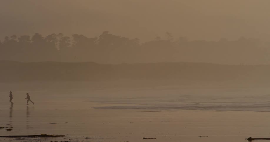 Two boys playing and running on the beach at dusk