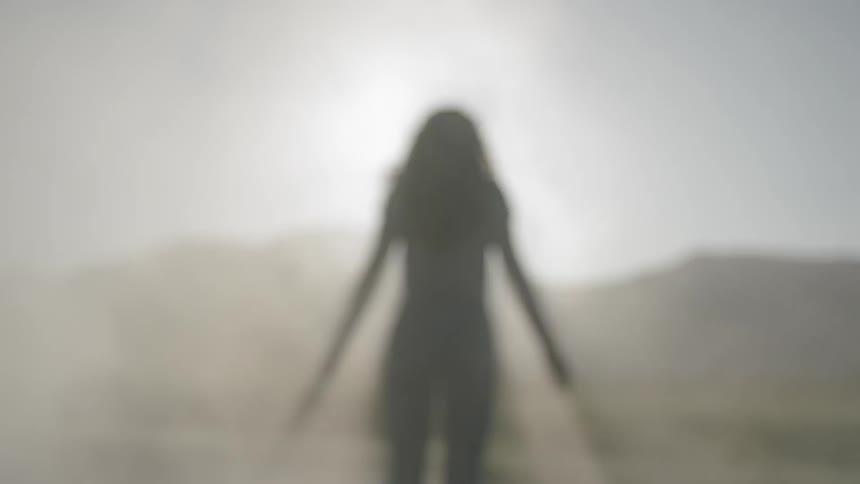 A woman stands and moves her arms in smoke