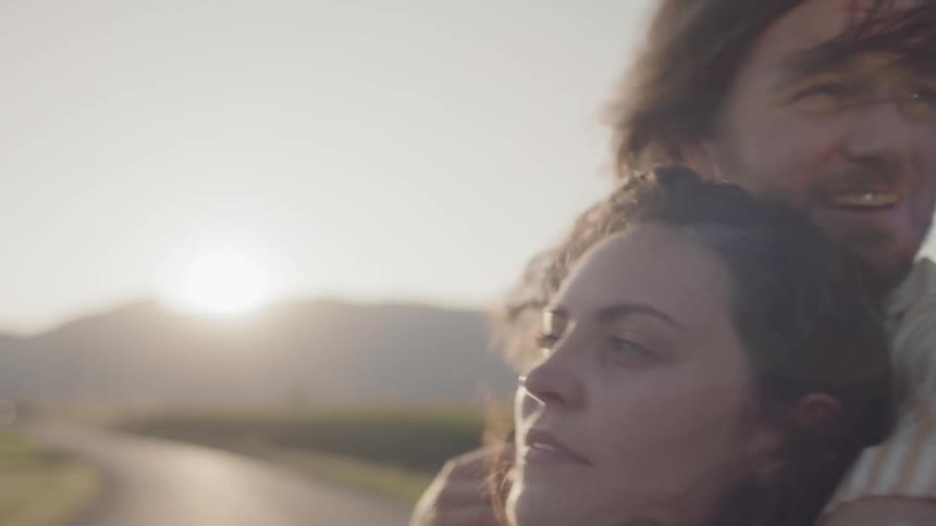 Man embraces a woman as they travel under a sunny sky