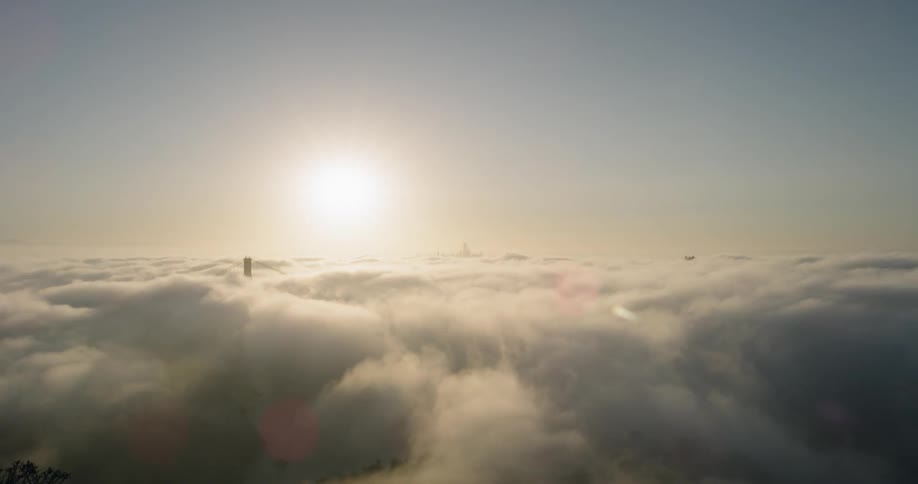 The sun above the clouds which hide a suspension bridge