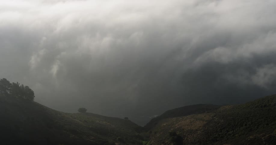 Clouds move across a hillside with a spare litter of trees