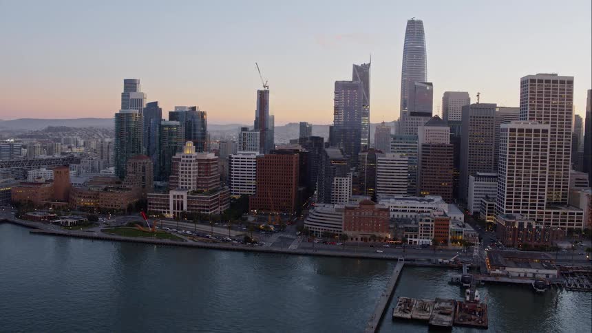Downtown city borders waterfront with mountains on the horizon at sunset