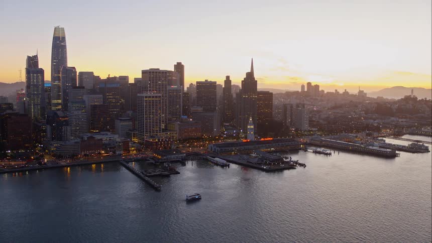 Skyline of the illuminated city next to the sea while the sun goes down