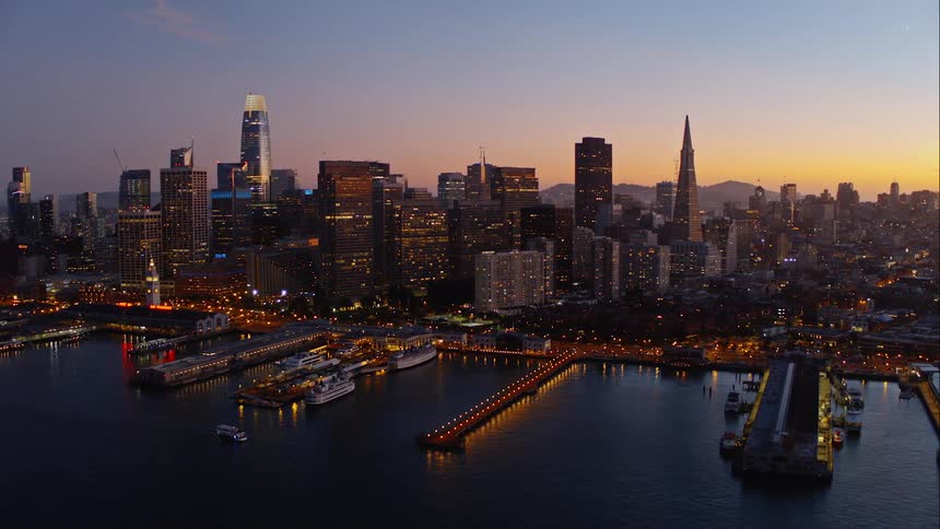 Lights shine along the piers and docks and skyscrapers in a waterfront city at sunset