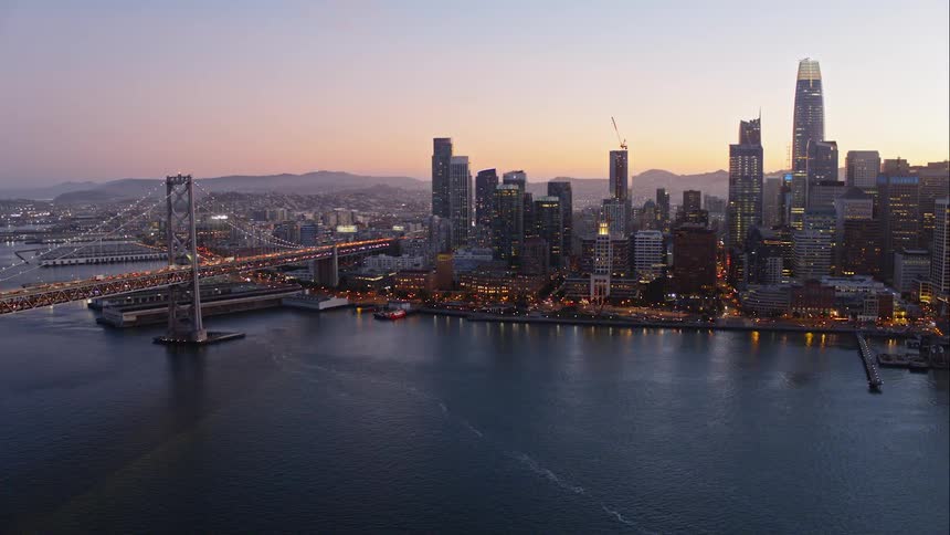 A city skyline with a large suspension bridge running over a river
