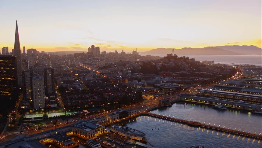The ships are docked near the large city at sunset