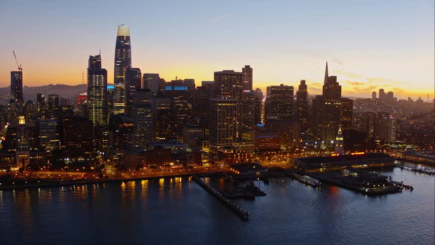 Brightly lit city bordering ocean at sunset