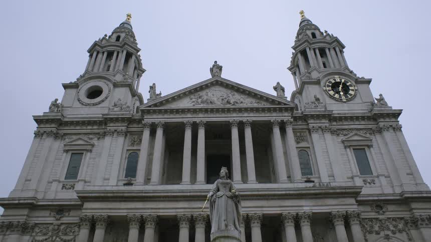 A large stone building has a statue and clock tower in front
