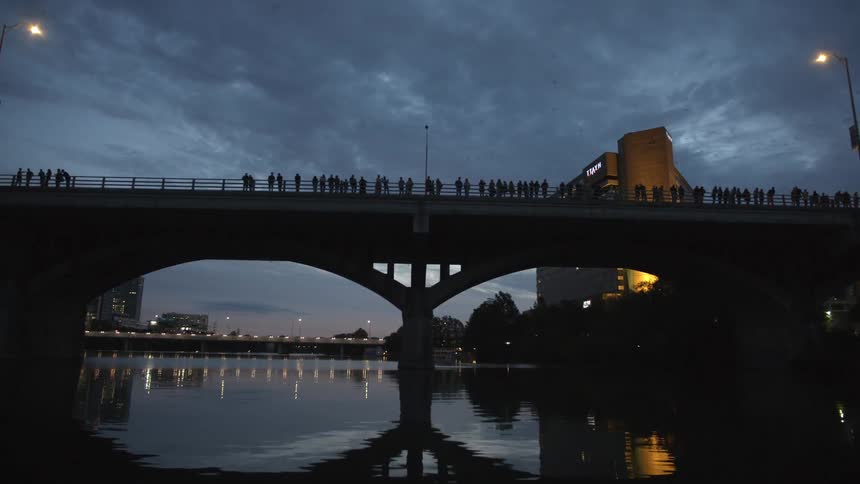 Many people are standing on a bridge taking photographs at sunset
