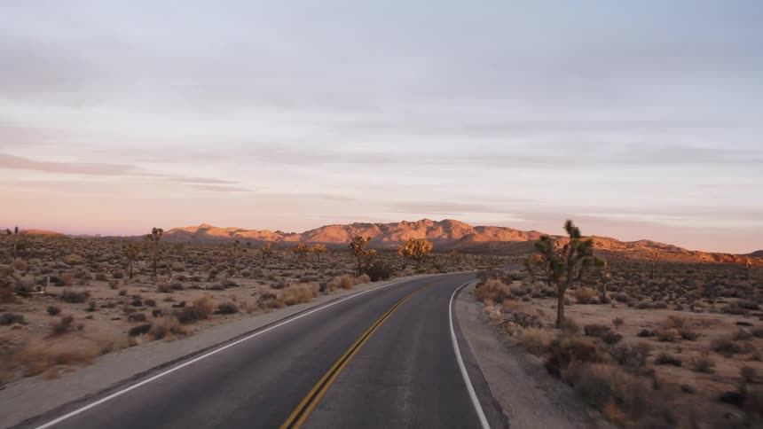 Driving along a winding desert road towards a mountain in the distance