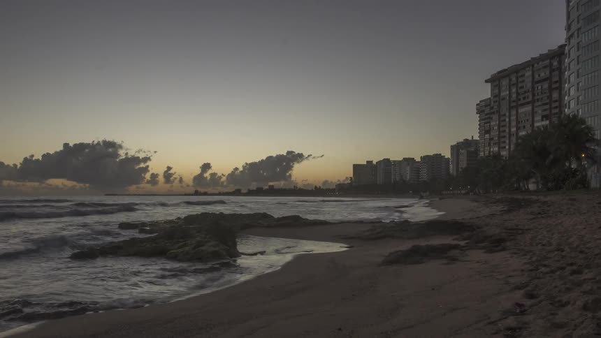 Time lapse of a row of buildings by the water as waves crash on the sand